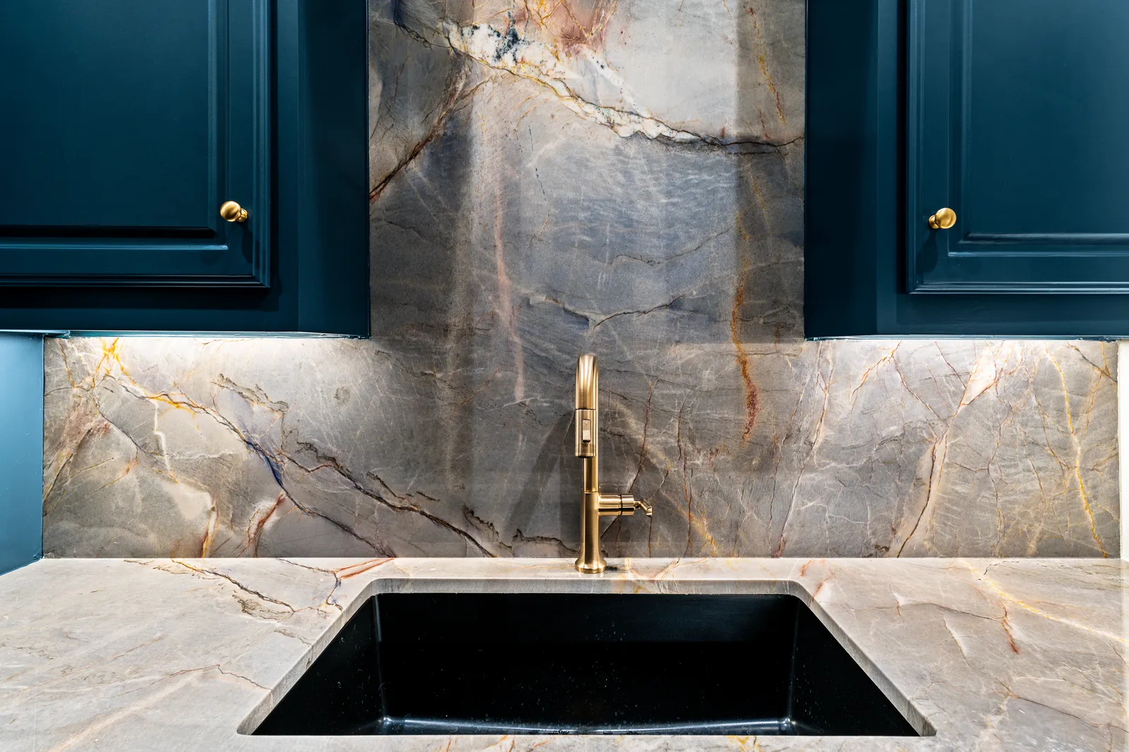 Ijen Blue quartzite counters and full-height slab backsplash with a brass faucet and black undermount sink on navy cabinetry, fabricated and installed by Dallas Countertop in Dallas, TX